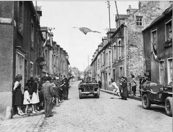 U.S. VII Corps jeep passing under French flag during the liberation of Carentan, 1944